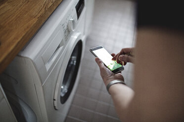 Ausgeschnittenes Bild einer älteren Frau, die im Badezimmer zu Hause ein Mobiltelefon benutzt - MASF07387