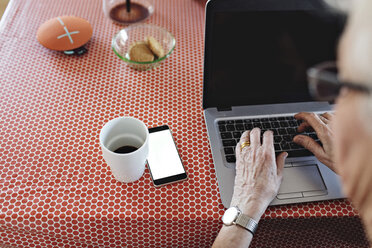 Hohe Winkel Ansicht der älteren Frau mit Laptop von Smartphone und Kaffeetasse auf Esstisch zu Hause - MASF07391