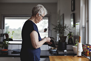 Seitenansicht einer älteren Frau, die ein digitales Tablet in der Küche zu Hause auflädt - MASF07409