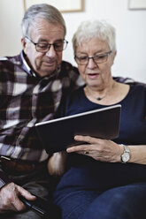 Senior couple sharing digital tablet against wall at home - MASF07428