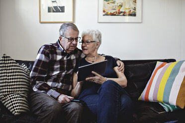 Älteres Ehepaar sitzt auf dem Sofa und teilt sich ein digitales Tablet an der Wand zu Hause - MASF07429