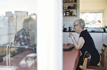 Seitenansicht eines älteren Paares, das am Esstisch sitzt, durch ein Fenster gesehen - MASF07432