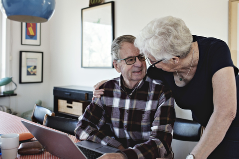 Lächelndes Seniorenpaar mit Laptop am Esstisch, lizenzfreies Stockfoto