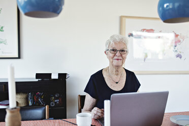Porträt einer lächelnden älteren Frau im Ruhestand, die mit einem Laptop am Esstisch sitzt - MASF07451