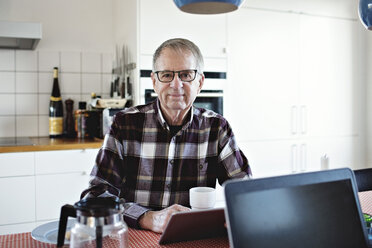 Porträt eines selbstbewussten älteren Mannes, der mit einem digitalen Tablet am Esstisch sitzt - MASF07452