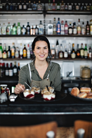 Porträt einer lächelnden Besitzerin mit Dessert an der Theke, lizenzfreies Stockfoto