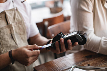 Owner using credit card reader while standing by male customer at table - MASF07477