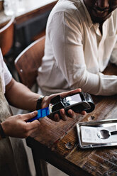 Cropped image of owner using credit card reader by customers at table in restaurant - MASF07479