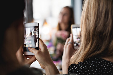 Frauen fotografieren Freund durch Smartphones am Esstisch im Restaurant - MASF07499