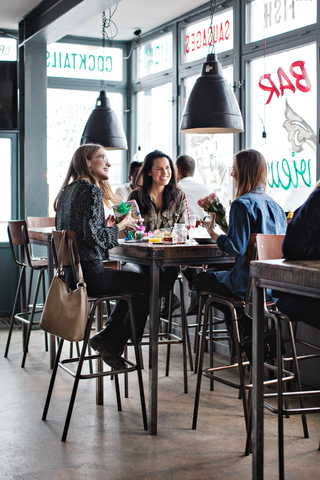 Lächelnde Freundinnen in voller Länge, die mit Geburtstagsgeschenken am Esstisch im Restaurant sitzen, lizenzfreies Stockfoto