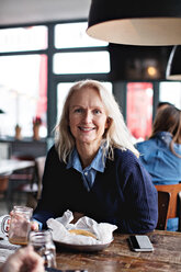 Porträt einer lächelnden reifen Frau, die am Esstisch im Restaurant sitzt - MASF07524