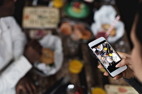 Abgeschnittenes Bild einer Frau, die Essen auf dem Esstisch eines Restaurants fotografiert, lizenzfreies Stockfoto