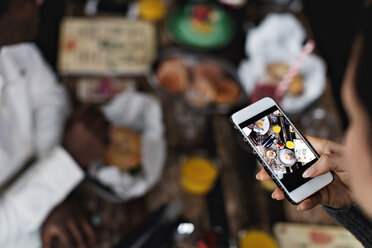 Abgeschnittenes Bild einer Frau, die Essen auf dem Esstisch eines Restaurants fotografiert - MASF07532