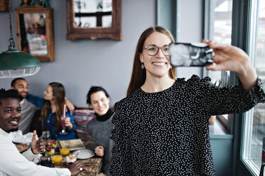 Smiling young woman taking selfie with friends sitting at restaurant - MASF07542