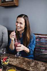 Lächelnde junge Frau, die in einem Restaurant am Tisch sitzt und etwas trinkt - MASF07550