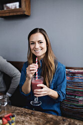 Porträt eines lächelnden jungen Kunden, der ein Getränk zu sich nimmt, während er am Esstisch im Restaurant sitzt - MASF07551