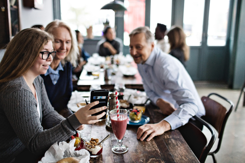 Lächelnde Tochter, die ein Selfie mit ihren Eltern macht, während sie am Tisch im Restaurant sitzt, lizenzfreies Stockfoto