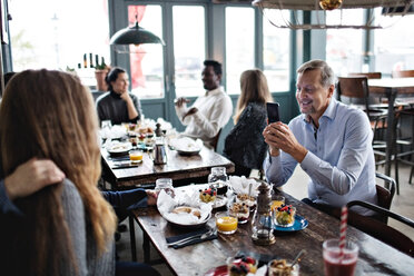 Mann fotografiert Frauen, während Freunde in einem Restaurant am Tisch sitzen - MASF07556