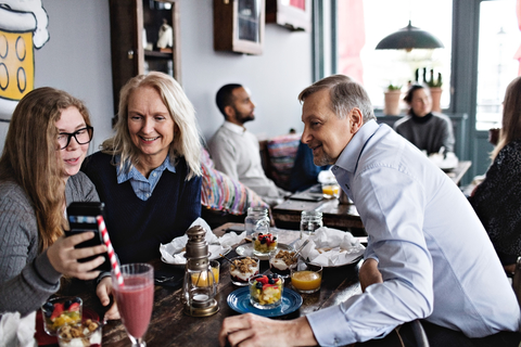 Lächelnde Tochter, die ein Selfie mit ihren Eltern macht, während sie am Tisch im Restaurant sitzt, lizenzfreies Stockfoto