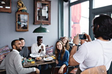 Der Besitzer fotografiert lächelnde Freunde mit dem Handy am Tisch im Restaurant - MASF07562