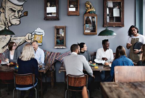 Eigentümer im Gespräch mit multiethnischen Freunden, während die Familie am Tisch im Restaurant bruncht - MASF07568