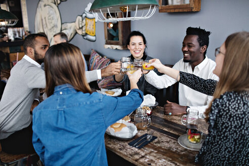 Glückliche Freunde stoßen auf ein Getränk an, während sie am Esstisch im Restaurant sitzen - MASF07572