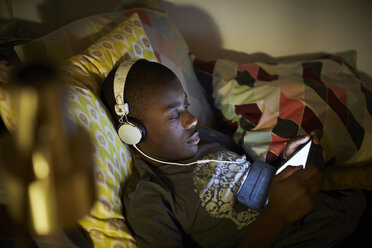 High angle view of boy wearing headphones and using digital tablet while lying on bed - MASF07581