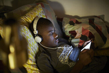 Hochformatiger Blick auf einen Jungen, der Kopfhörer trägt und ein digitales Tablet benutzt, während er auf dem Bett liegt - MASF07581