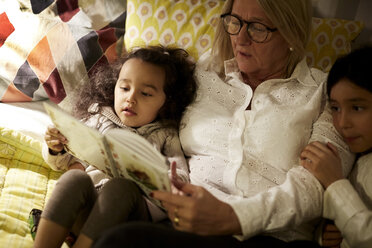 High angle view of grandmother reading book to granddaughters while lying on bed at home - MASF07584