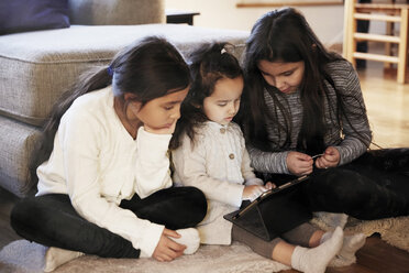 Schwestern, die zu Hause auf dem Teppich sitzend auf ein digitales Tablet schauen - MASF07601