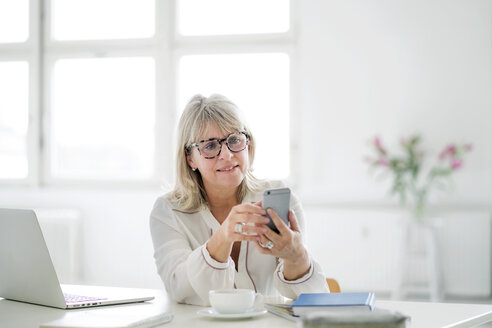 Mature businesswoman looking at cell phone at desk - HHLMF00248