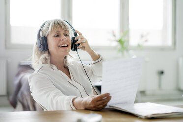 Lachende reife Geschäftsfrau mit Kopfhörern, die ein Dokument am Schreibtisch betrachtet - HHLMF00254