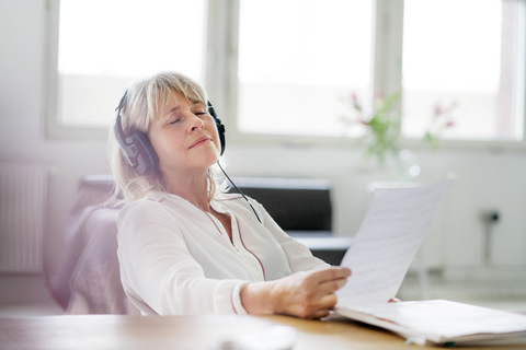 Entspannte reife Geschäftsfrau mit Kopfhörern am Schreibtisch, lizenzfreies Stockfoto