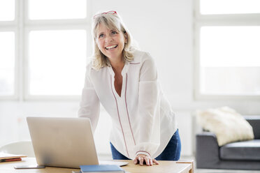 Porträt einer glücklichen reifen Geschäftsfrau mit Laptop auf dem Schreibtisch - HHLMF00257