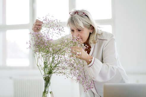 Mature woman with laptop caring for flowers - HHLMF00261