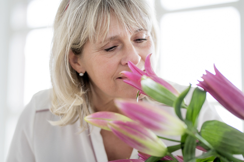 Reife Frau riecht an einem Blumenstrauß, lizenzfreies Stockfoto