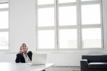 Smiling mature businesswoman with laptop at desk in the office looking up - HHLMF00267