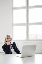 Porträt einer lächelnden reifen Geschäftsfrau mit Laptop am Schreibtisch im Büro - HHLMF00268