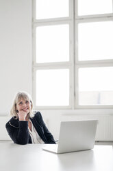 Portrait of smiling mature businesswoman with laptop at desk in the office - HHLMF00268