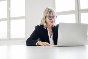 Lächelnde reife Geschäftsfrau arbeitet am Laptop am Schreibtisch im Büro - HHLMF00270