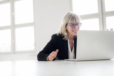 Lächelnde reife Geschäftsfrau arbeitet am Laptop am Schreibtisch im Büro - HHLMF00271