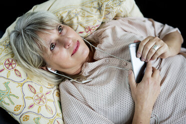 Smiling mature woman lying down with cell phone and earphones - HHLMF00286