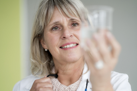 Lächelnde reife Frau hält ein Glas Wasser, lizenzfreies Stockfoto