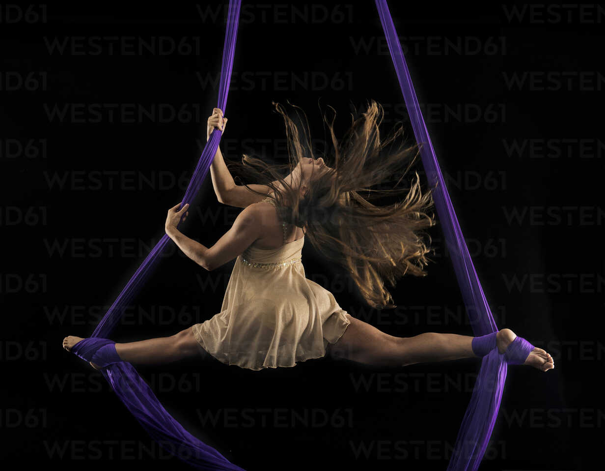 Young female aerial acrobat doing the splits with feet wrapped in