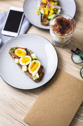 Vegetarian breakfast with bread, eggs and tomato slices on plate, latte macchiato, smartphone, notebook - GIOF03941