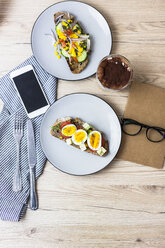 Vegetarian breakfast with bread, eggs and tomato slices on plate, latte macchiato, smartphone, notebook - GIOF03942