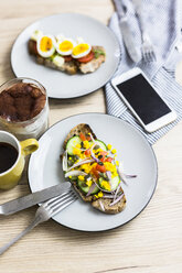 Vegetarian breakfast with bread, eggs and cucumber slices on plate, smartphone, latte macchiato, coffee cup - GIOF03943