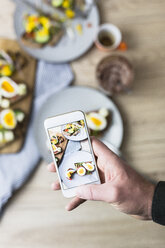 Mann hält Smartphone mit Foto von vegetarischem Frühstück mit Brot und Eiern - GIOF03944