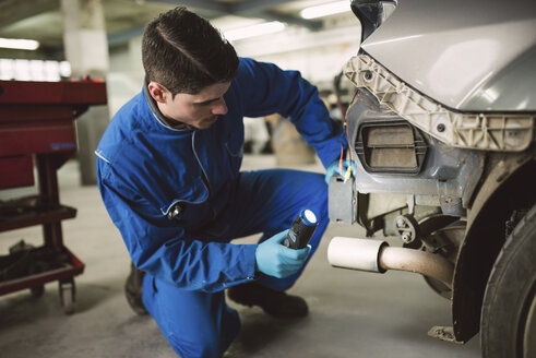Mechaniker inspiziert ein Auto mit einer Taschenlampe in einer Werkstatt - RAEF01992