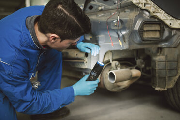 Mechaniker inspiziert ein Auto mit einer Taschenlampe in einer Werkstatt - RAEF01993